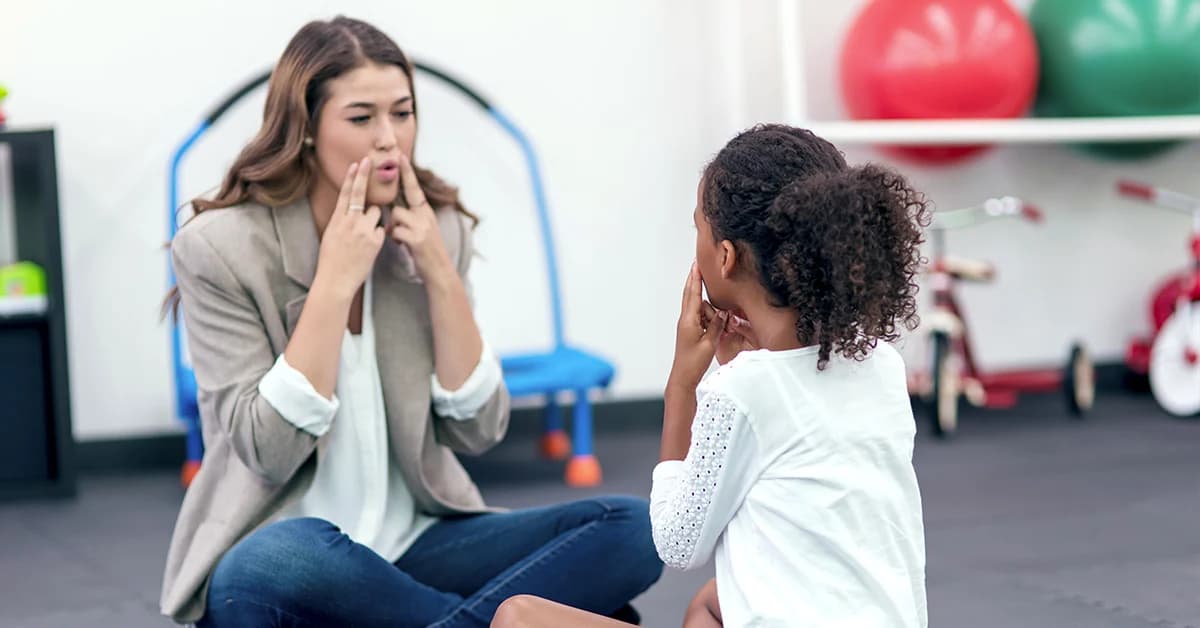 A speech therapist modeling a sound for a young girl during a therapy session